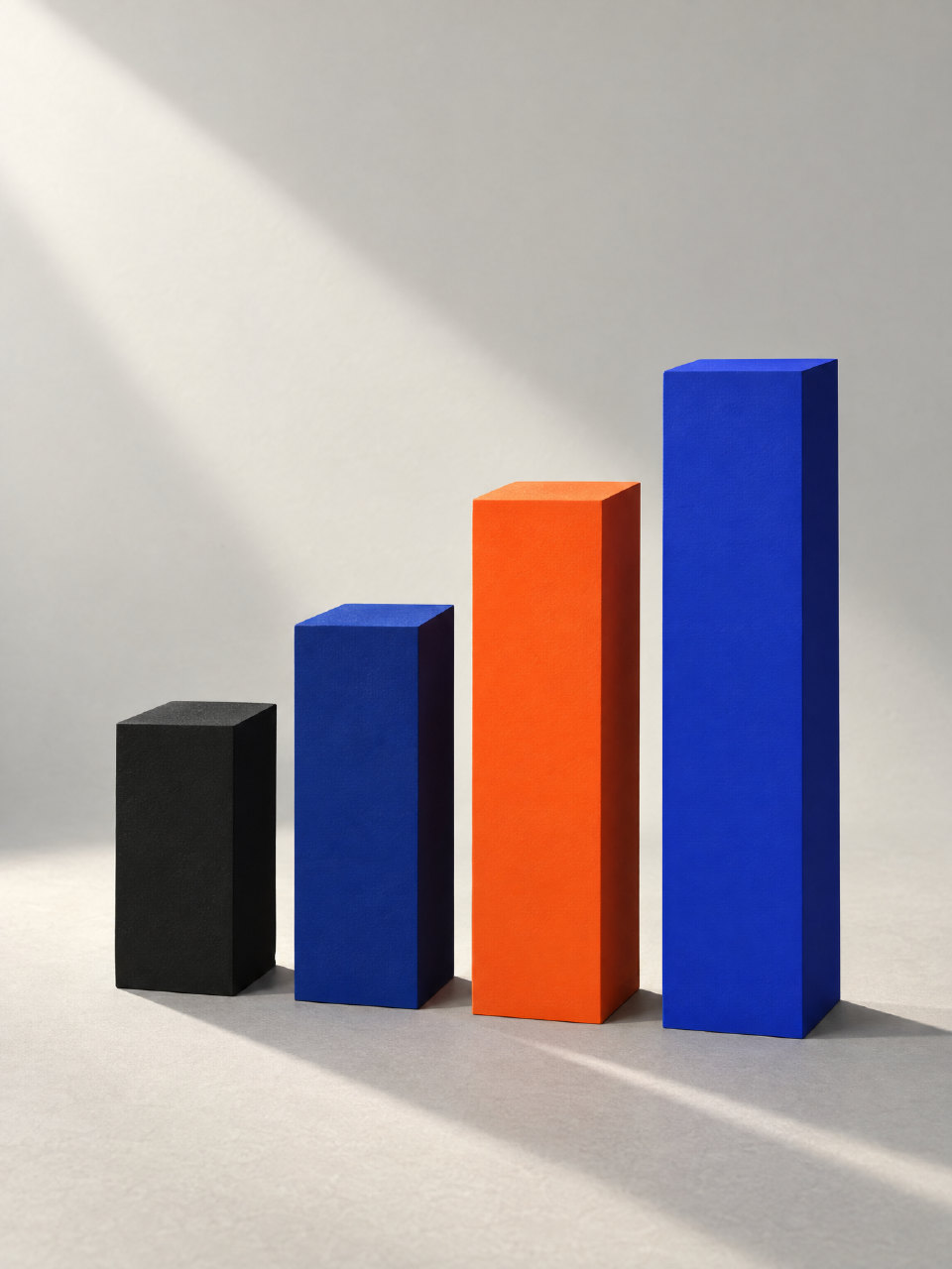 Four painted blocks in charcoal, navy, orange and ultramarine, rising from left to right in low sunlight.